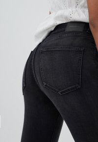 Musta denim-farkut, joissa istuva malli, tavalliset takataskut ja näkyvä merkkilappu vyötäröllä.