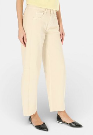 Kobieta nosząca kremowe, szerokie spodnie z wysokim stanem i przednimi kieszeniami, w połączeniu z czarnymi balerinami z ostrym noskiem i jasnokropkowym topem.