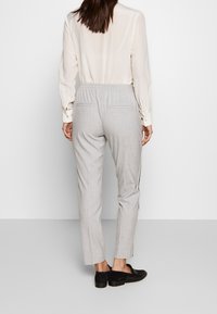Ljust grå byxor med en texturerad tyg, elastisk midja, sidofickor och kontrasterande svarta sidostreck, matchat med en krämfärgad blus.