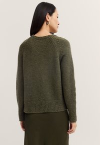 Olivgrüner, gestrickter Pullover mit strukturiertem Finish, geripptem Saum und überschnittenen Schultern, kombiniert mit einem dunkelolivfarbenen Rock.