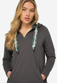 Hoodie gris en tissu doux, avec un col en V, des manches longues et des cordons de serrage à motif vert. Il comprend une poche avant.