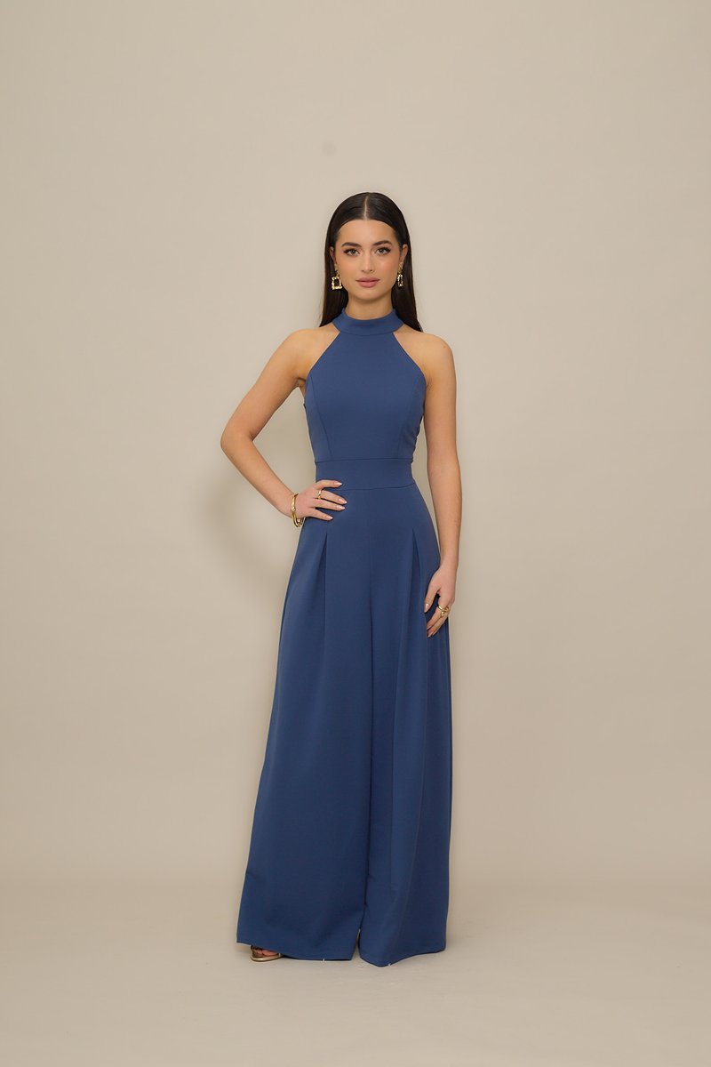 Ναυτικό μπλε ολόσωμη φόρμα με λαιμόκοψη halter, εφαρμοστή μπούστα και παντελόνια φαρδιάς γραμμής. Λείο ύφασμα, πιετέ λεπτομέρειες και μίνιμαλ στοιχεία σχεδιασμού.