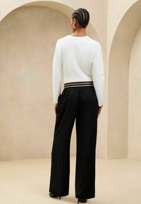 Pantaloni neri a gamba larga con vita arricciata e strisce orizzontali a contrasto, abbinati a una maglietta bianca a maniche lunghe.