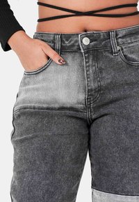 Jeans de mezclilla de tiro alto, en negro y gris, con un patrón deslavado, diseño de cinco bolsillos y cierre de botón metálico. Acabado de tejido texturizado.