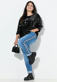 Top negro con lentejuelas y mangas tres cuartos, jeans azul claro con tiras de logo en los laterales y botas de combate negras de suela gruesa. Incluye un pequeño bolso negro.