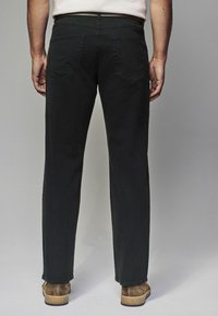 Pantalones de mezclilla negros con corte recto, que cuentan con dos bolsillos traseros y una cinturilla limpia. Llevados con zapatos de ante marrones.