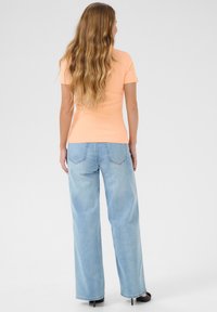 T-shirt arancione fitted a costine abbinato a jeans a gamba larga azzurri, che mostrano una silhouette rilassata e una morbida texture in denim.