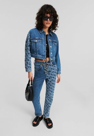 Ensemble de veste en denim coupée et de jeans ; tissu bleu avec des accents à motifs. Comprend des accessoires en argent, un devant à lacets, ainsi qu'un sac noir et des sandales.