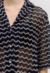 Herrenhemd mit kurzen Ärmeln in marineblau und creme mit Spitzenstruktur, Kragen und vorderer Knopfleiste. Zickzackmuster über die gesamte Fläche.
