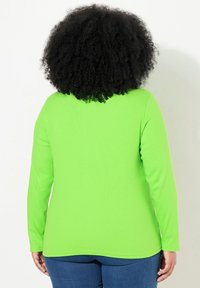 Langärmliges Shirt in kräftigem Limettengrün, mit gerippter Textur und lässigem Schnitt. Der Saum endet auf Hüfthöhe und passt gut zu dunkelblauen Jeans.