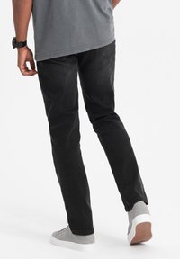 Pantaloni in denim neri con vestibilità slim, texture ruvida e dettagli di cucitura sottili. Abbinati a scarpe alte grigie e una maglietta grigia.