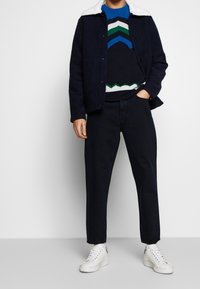 Navy wool jacket with faux fur collar, knit sweater featuring blue, green, and white zigzag patterns, paired with dark pants and white sneakers.