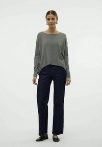 Ανοιχτό γκρι, μακρυμάνικο πουλόβερ με χαλαρή γραμμή, συνδυασμένο με σκούρο μπλε τζιν σε ίσια γραμμή και μαύρες μπαλαρίνες, σε φόντο λευκό.