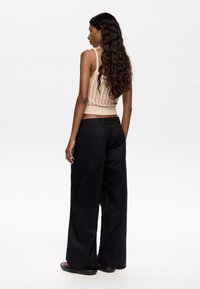 Knit tank top with vertical stripes in cream, orange, and yellow; paired with high-waisted black wide-leg pants.