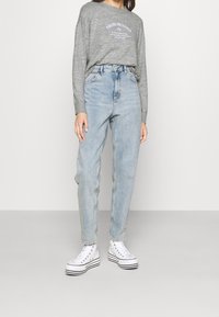 Sweatshirt gris avec texte imprimé, associé à un jean taille haute bleu clair. Baskets blanches avec des rayures noires sur la semelle.