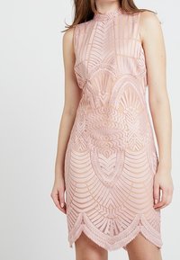 Robe courte rose avec un col montant, présentant des motifs géométriques en dentelle complexes et un ourlet festonné. Design sans manches.