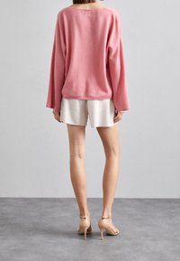 Rosa Langarm-Pullover mit weitem Ausschnitt, kombiniert mit hellen Shorts und beigen High-Heels. Weicher Stoff, lässige Passform.