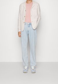 Jasnoszary dzianinowy blezer z naszywanymi kieszeniami, różowy t-shirt, luźne jasnoniebieskie dżinsy oraz niebieskie buty sportowe z kremowymi akcentami.