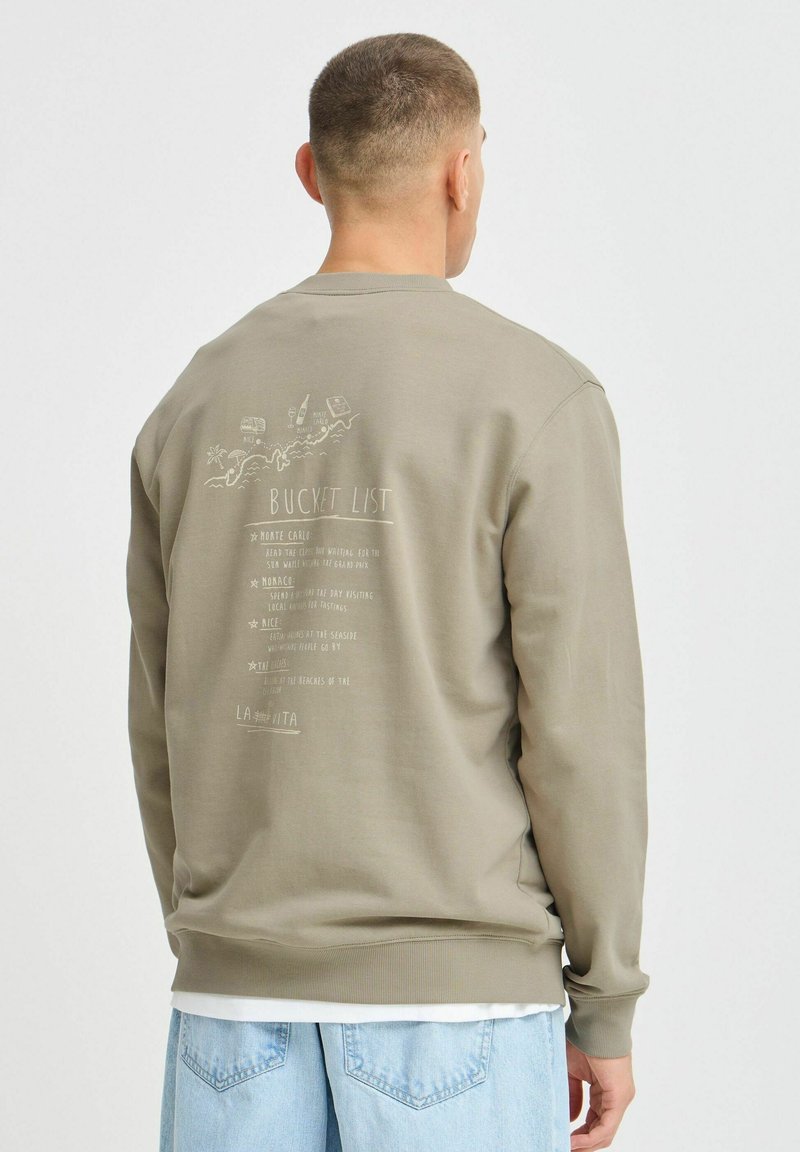 Sweatshirt vert olive en tissu doux, avec une impression graphique plus claire au dos comportant le texte "Bucket List" et des accents.