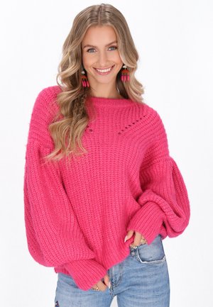 Rosa gestrickter Pullover mit lockerem Schnitt, gerippter Textur, übergroßen Ärmeln und einem runden Ausschnitt, kombiniert mit Jeans.