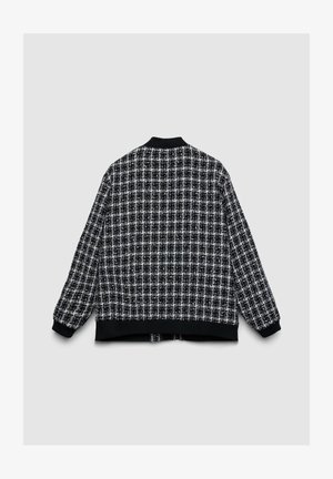 Blouson aviateur à carreaux noir et blanc avec col et poignets en maille, présentant un tissu texturé et une coupe droite.