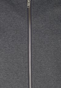 Gros plan sur une fermeture éclair en métal argenté sur un tissu texturé gris foncé, entièrement fermée.