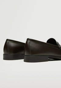 Pari tummanruskeita nahkaloferia matalilla mustilla koroilla, esiteltyinä takaa ja sivulta vaaleaa taustaa vasten.