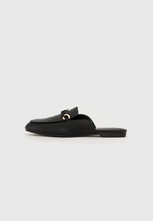 Czarny skórzany mule na płaskim obcasie z dekoracyjnym czarnym łańcuchem na cholewce, widok z boku na białym tle.