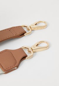 Pruun nahast rihm kuldsete metallist klambritega. Tekstuuriga viimistlus, nähtavad õmblused ja graveeritud bränding metalldetailidel.