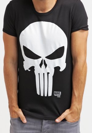 Person trägt ein schwarzes T-Shirt mit großem weißem Punisher-Schädel-Logo und kleinem Marvel-Logo unten rechts. Hände in den Taschen.