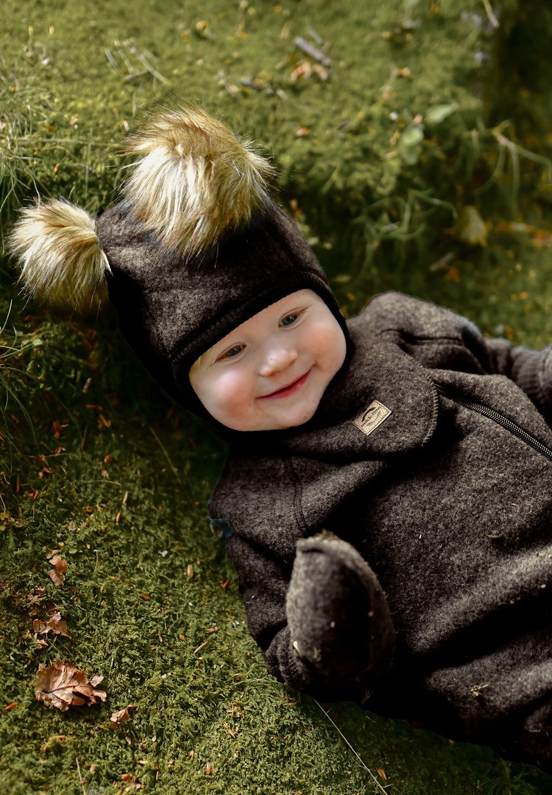 Tamno smeđi vuneni kombinezon s kapuljačom ukrašenom krznom i zaobljenim ušima. Mekana tekstura, zatvarač i mali logotip na prsima.