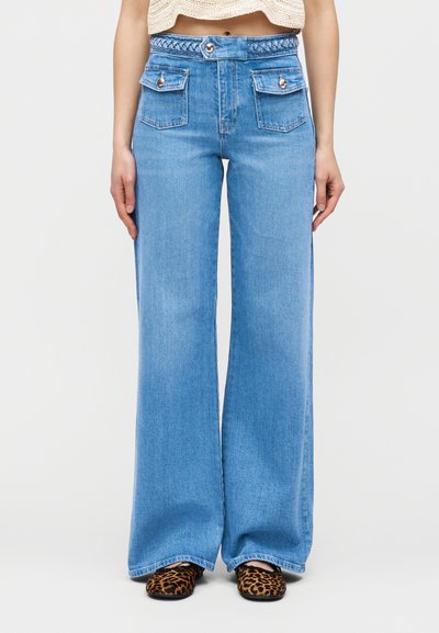Φαρδιά τζιν παντελόνια ψηλής μέσης σε ανοιχτό μπλε χρώμα με πλεκτή ζώνη στη μέση, δύο εμπρόσθιες τσέπες με καπάκια και κουμπιά, συνδυασμένα με παπούτσια με λεοπάρ μοτίβο.