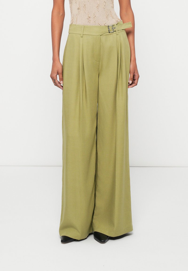 Πλατιά παντελόνια σε ελιά πράσινο ύφασμα με πιέτες, ζώνη με ασημένια αγκράφα και λεία υφή. Φοριέται με μαύρες γόβες.