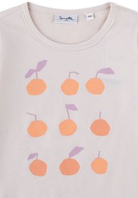 Helles beiges T-Shirt mit neun orangefarbenen Kreisen und lila Stielen und Blättern, die in einem Gittermuster bedruckt sind. Weiches Baumwollmaterial, runder Ausschnitt.