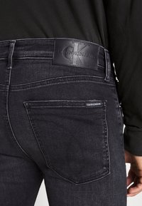 Son unos jeans de mezclilla oscura con un parche de cuero de Calvin Klein Jeans en la parte trasera, detalles de costura sutiles y un diseño ajustado.