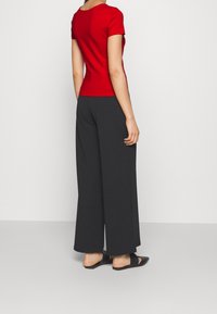 Top ajustado rojo de manga corta combinado con pantalones anchos negros y sueltos, y zapatos negros de punta abierta, sobre un fondo claro y liso.