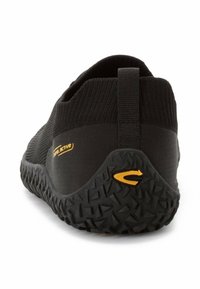 Black athletic shoe with a textured sole, featuring a flexible fabric upper and a yellow logo on the side. Subtle design lines at the heel.