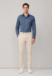 Lichtblauw overhemd met knopen, beige broek en witte sneakers. Gladde stof, klassieke kraag en knoopaccenten op het shirt en de broek.