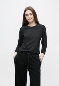 Crna dugopruga majica s okruglim izrezom i suptilnim prednjim vezom, uparena s crnim trenirkama koje imaju prugaste bočne naglaske.