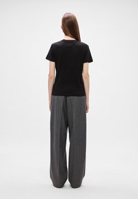 Μαύρο κοντομάνικο μπλουζάκι συνδυασμένο με γκρι παντελόνι wide-leg με ρίγες, και τα δύο διαθέτουν απλές σχεδίασεις και χαλαρή εφαρμογή.