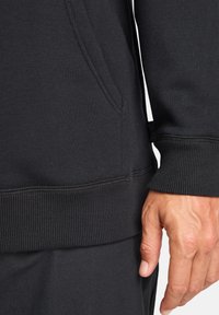 Felpa nera con orlo e polsini a costine, texture liscia e tasca frontale. Dettagli ravvicinati del tessuto e delle cuciture.