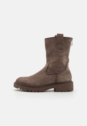 Bottine en suède marron avec un bout arrondi, des coutures latérales, une languette à l'arrière et une semelle robuste pour l'adhérence. Détail de fermeture éclair sur le côté.