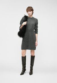 Vestido de malha cinza com mangas longas e decote redondo, combinado com botas pretas brilhantes até ao joelho e uma bolsa preta texturizada.