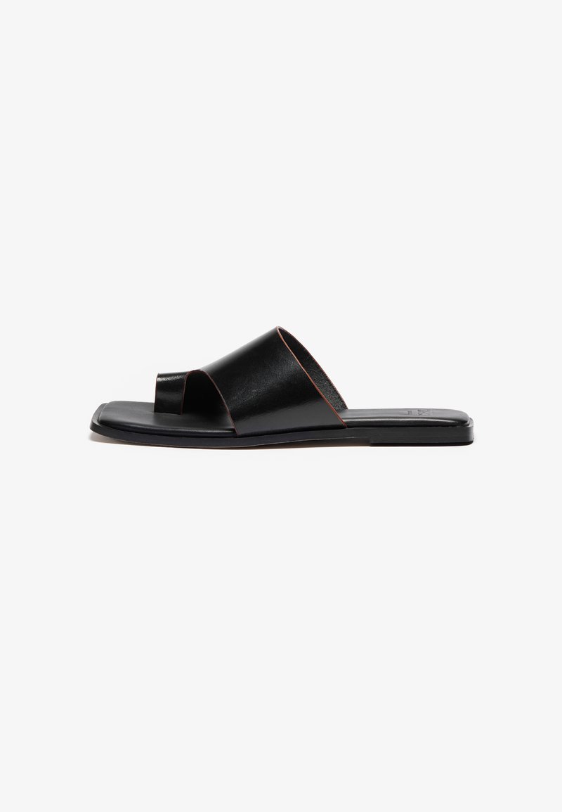 Sandale en cuir noir à enfiler au design minimaliste, avec une ouverture au niveau des orteils et des brides croisées. Texture lisse et semelle plate.