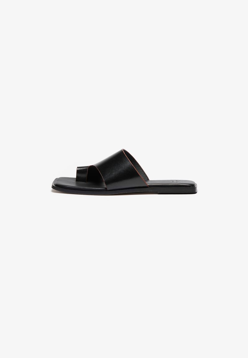 Sandale en cuir noir à enfiler au design minimaliste, avec une ouverture au niveau des orteils et des brides croisées. Texture lisse et semelle plate.