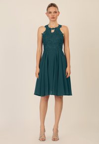 Teal jurk met een aansluitend kanten lijfje met bloemmotieven, een keyhole halslijn en een uitlopende rok van een lichte stof.