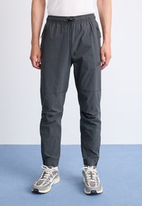 Graue Jogginghose mit einem Kordelzugbund, Reißverschlusstaschen und schmalem Schnitt. Hergestellt aus leichtem, glattem Material mit dezentem Branding.