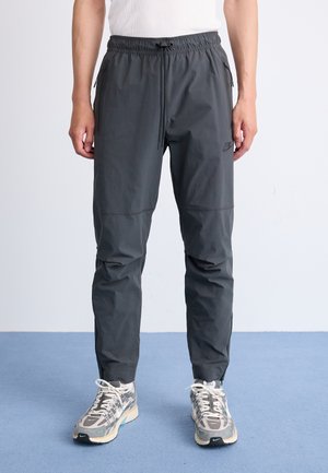 Pantalons de jogging gris avec un cordon de serrage à la taille, poches zippées et coupe fuselée. Fabriqués en tissu léger et lisse avec un branding subtil.