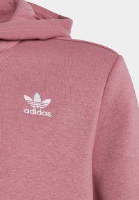 Růžová mikina s texturovanou tkaninou, na hrudi s bílým logem Adidas a s kapucí na stažení.