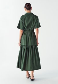 Abito midi in cotone verde con maniche corte, vita arricciata e gonna a strati. Texture liscia e vestibilità comoda. Sandali neri con cinturini.